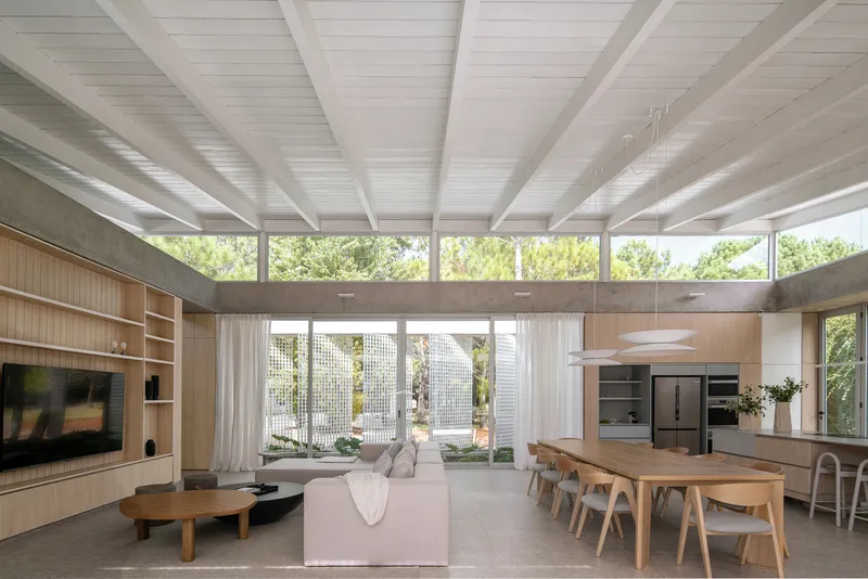 Open-plan living space with exposed concrete beams and clerestory windows overlooking greenery