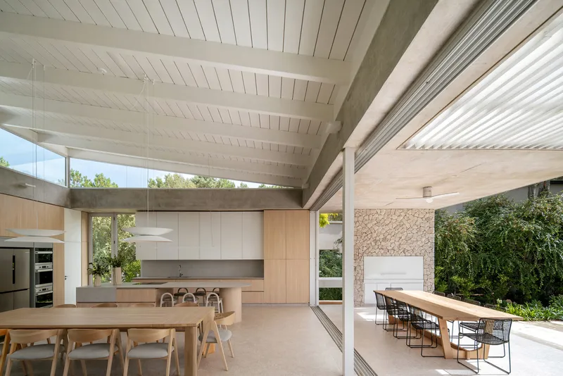 Open-plan kitchen and dining area with white timber ceiling and full-height glazing to the garden