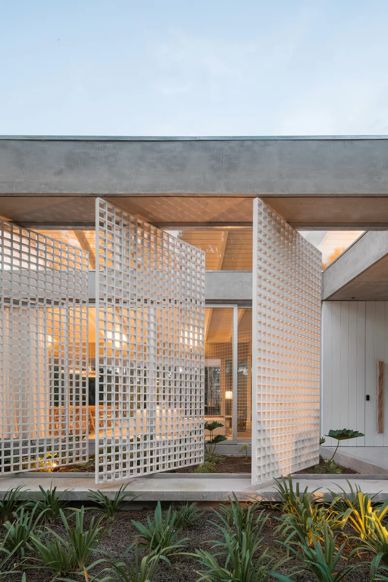 White lattice screens wrapping an entry courtyard with planted beds at dusk