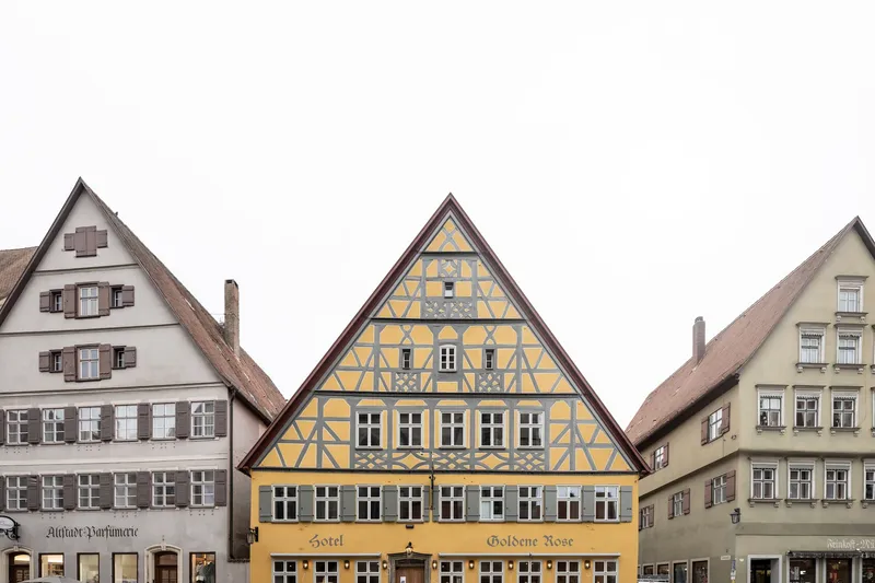 Yellow half-timbered facade with dark patterned infill flanked by neighboring gabled buildings under overcast sky
