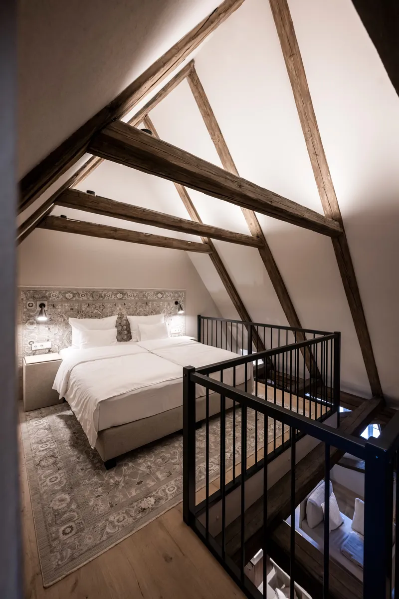 Gabled bedroom with exposed timber trusses and black metal stair railing in evening light