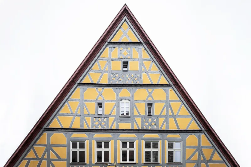 Centered view of the triangular timber-framed gable with yellow infill panels against an overcast sky
