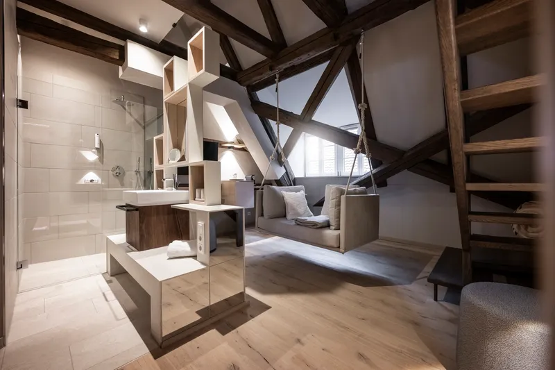 Open bathroom with glass shower enclosure and exposed timber trusses cutting diagonally through the volume