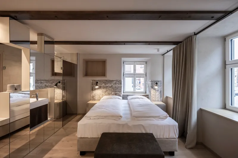 Bedroom with mirrored wardrobe partition and exposed stone wall backing the upholstered headboard