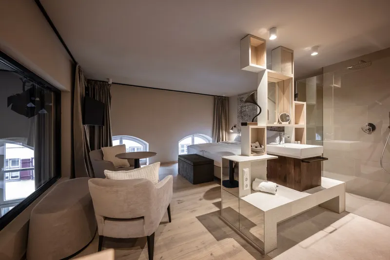 Open suite interior with glass-enclosed bathroom, illuminated timber shelving, and arched windows overlooking the street