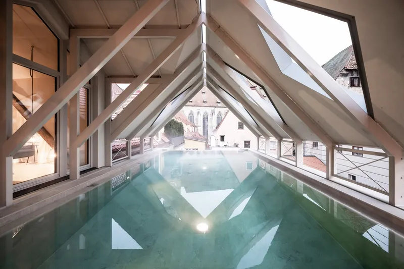 Long view of the rooftop pool framed by diagonal timber beams and continuous slope glazing