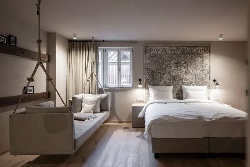 Guest room with rope-suspended bench seating and patterned wall hanging behind the bed