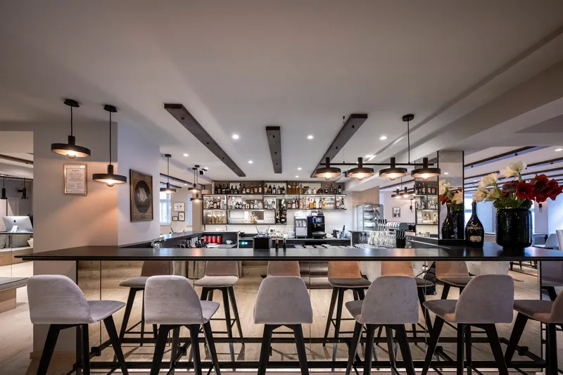 Bar counter with upholstered stools beneath dark timber ceiling beams and pendant lights