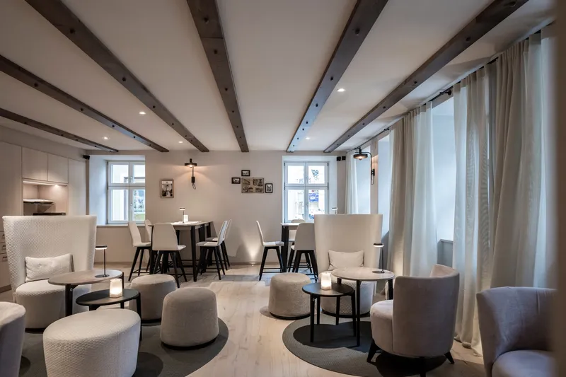 Lounge area with clustered seating groups under exposed ceiling beams and sheer curtains along windows