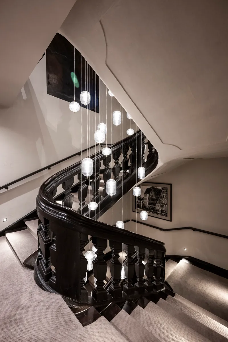 Curved staircase with black wood balustrade and cascading globe pendant lights in the stairwell