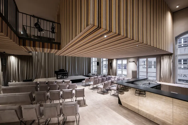 Performance hall with ribbed timber ceiling canopy descending over rows of seating and a mezzanine balcony