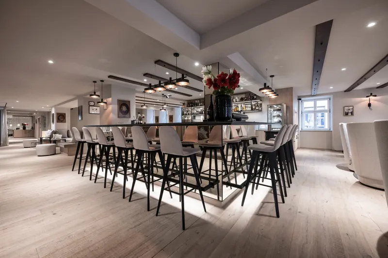 Central bar counter surrounded by high stools beneath linear pendant lights in an open lounge space