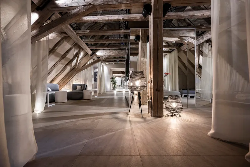 Attic interior with exposed timber trusses, concrete columns, and wicker pendant lights along a polished floor
