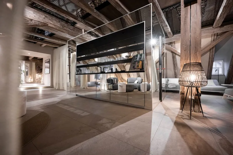 Freestanding glass cube partition beneath exposed timber rafters and mesh ceiling panels