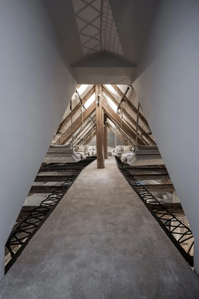 Central concrete walkway flanked by metal mesh decking under symmetrical timber roof trusses