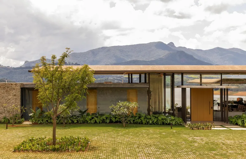 Glass-walled pavilion with overhanging timber roof set against distant mountains under overcast sky