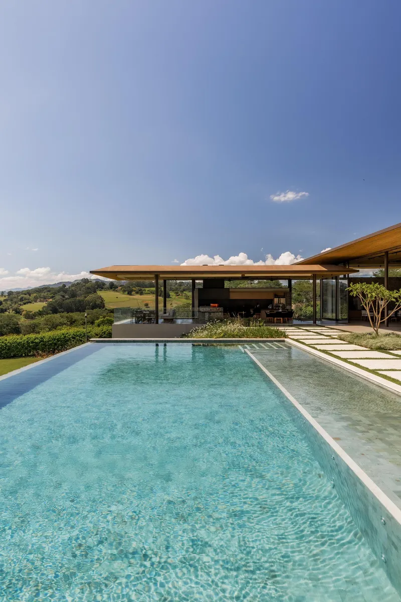 Infinity pool with pale limestone coping and grass-jointed pavers under a clear afternoon sky