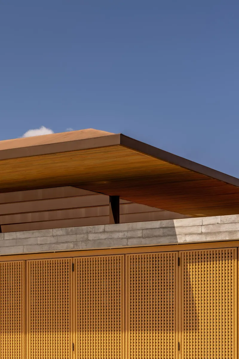 Detail of the angled timber roof eave and perforated wood screen facade at dusk