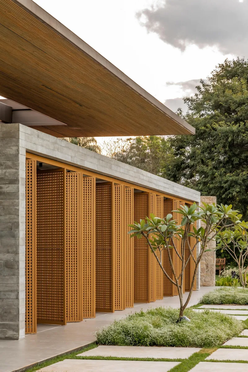 Perforated timber facade panels between concrete piers and planted beds with frangipani trees