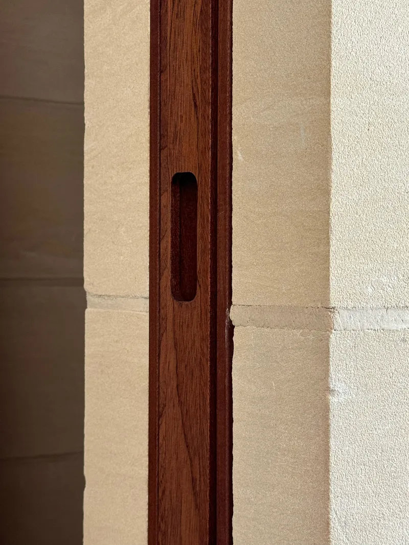 Detail of timber door pull recessed into the darkwood frame against a limestone wall in afternoon sunlight