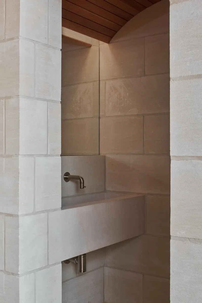 Limestone basin wall with bronze tap fixture beneath a timber ceiling soffit