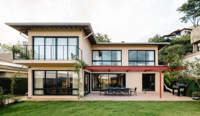Garden facade with covered terrace, exposed timber roof beams and large gridded glass doors under cloudy skies