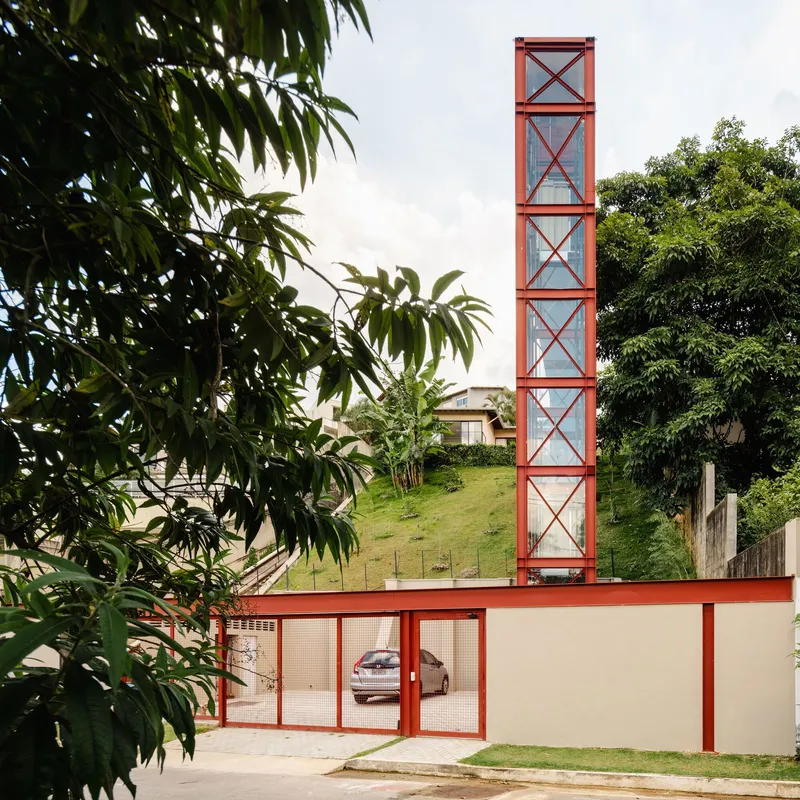 Street facade with red steel frame tower and mesh gate framed by overhanging tree branches