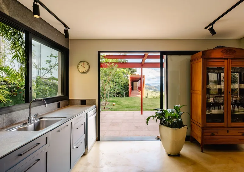 Kitchen view through open sliding door to exterior porch with red steel frame and hillside beyond