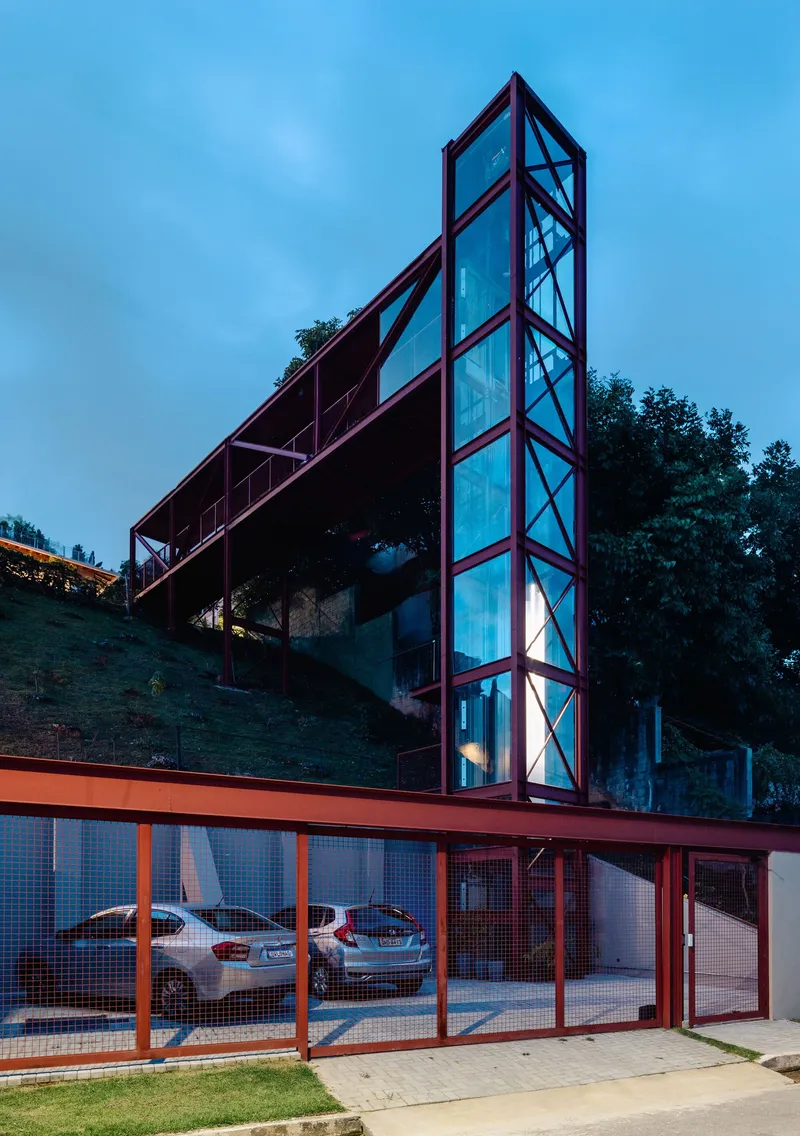 Street view of the red steel-framed tower rising above the mesh-fenced carport at dusk