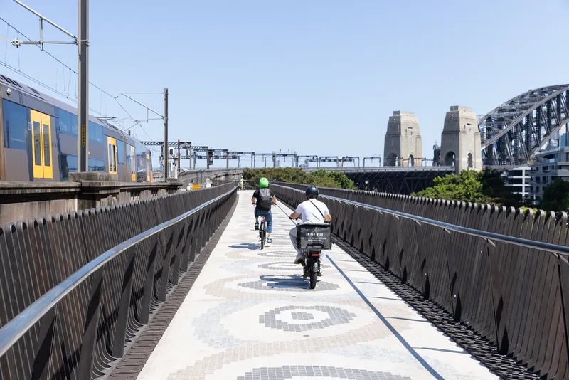 Pedestrian and cycle bridge with patterned concrete paving and vertical metal railings under clear afternoon sky