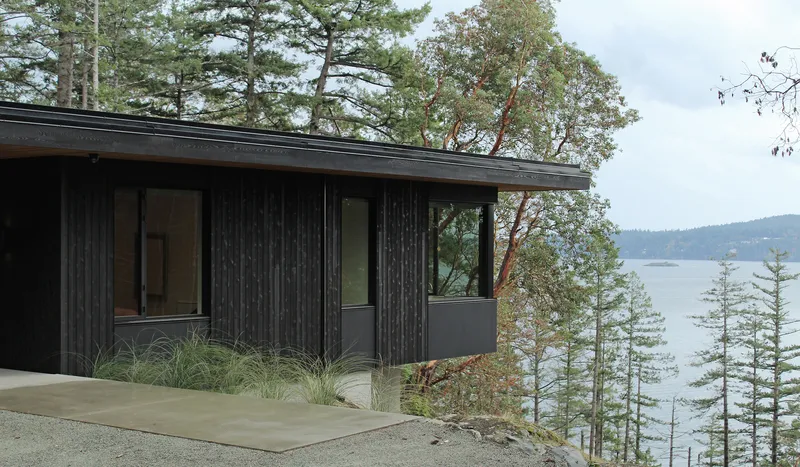Charred wood facade with concrete terrace overlooking a forested lakeside