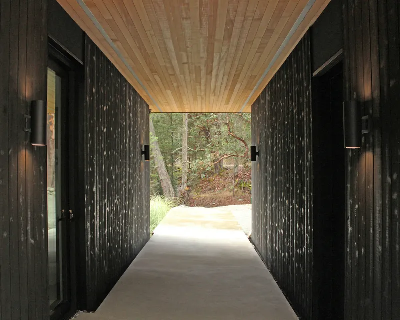 Entry corridor with wood plank ceiling framing view of arbutus trees beyond