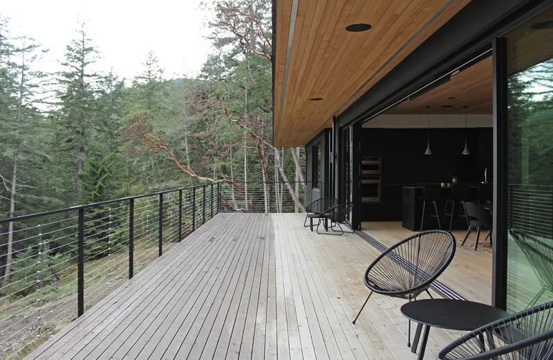 Timber deck with cable railing opening to forested slope through sliding glass doors