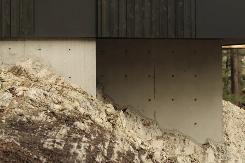Concrete foundation wall meeting exposed bedrock beneath charred timber cladding