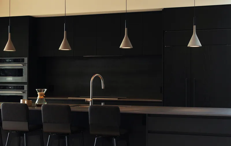 Kitchen island with conical pendant lights suspended over black cabinetry and timber countertop