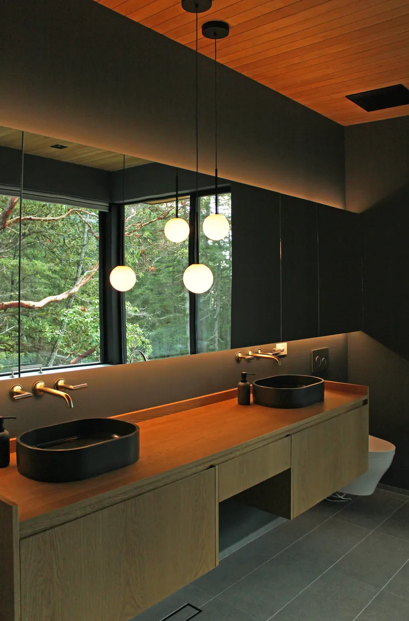 Bathroom vanity with timber counter and pendant globe lights facing forest through floor-to-ceiling glazing