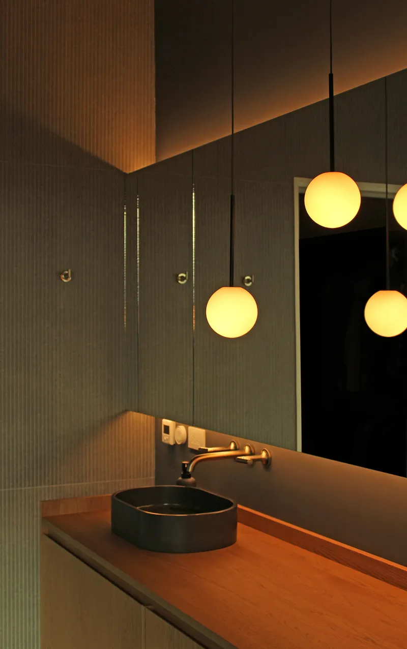 Close-up of circular basin and wall-mounted faucet with globe pendants reflected in mirror