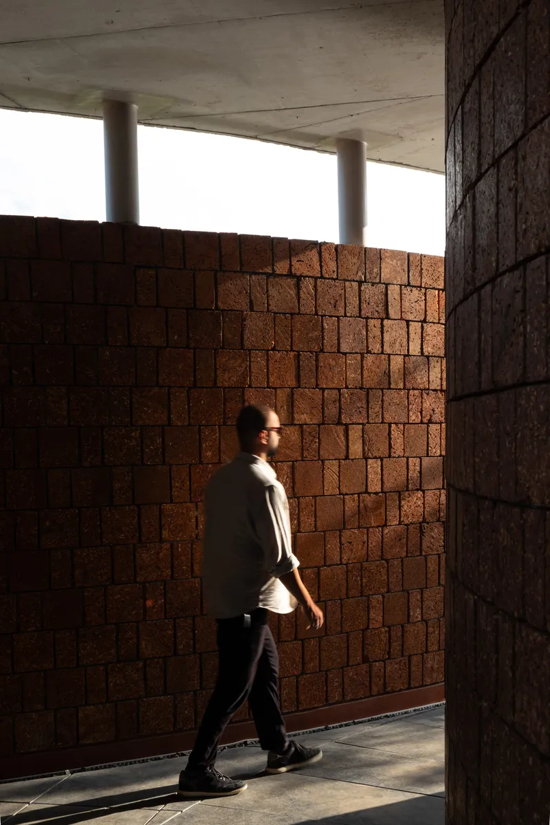 Interior corridor with figure walking past laterite brick walls beneath a concrete soffit with cylindrical columns