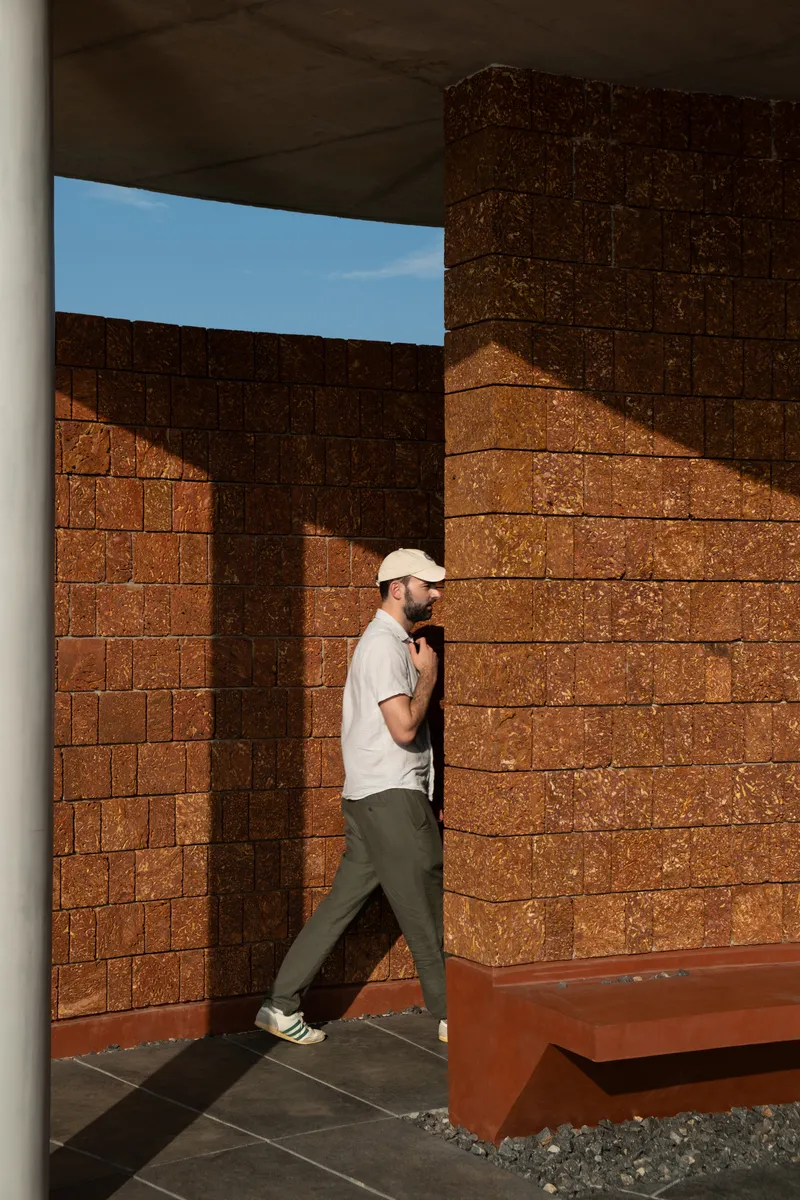 Visitor walking through courtyard framed by textured rammed earth walls in afternoon sunlight