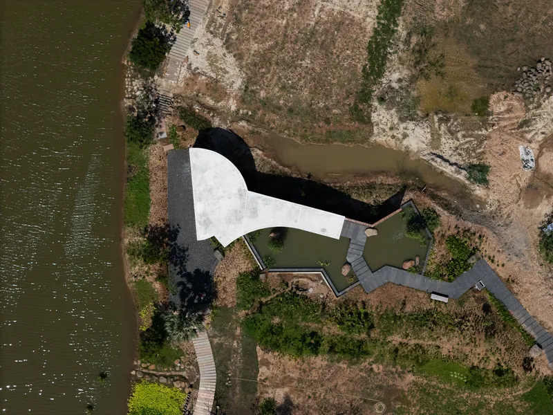 Aerial view of white curving roof structure adjacent to waterfront and wetland vegetation