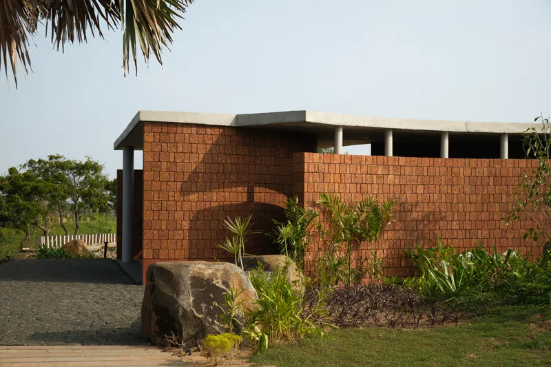 Red laterite brick wall with arched entry opening set among palm fronds and planted boulders