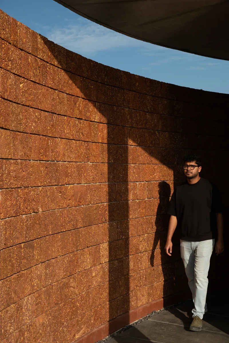 Curved laterite brick wall with vertical shadow pattern as a person walks beneath the overhang