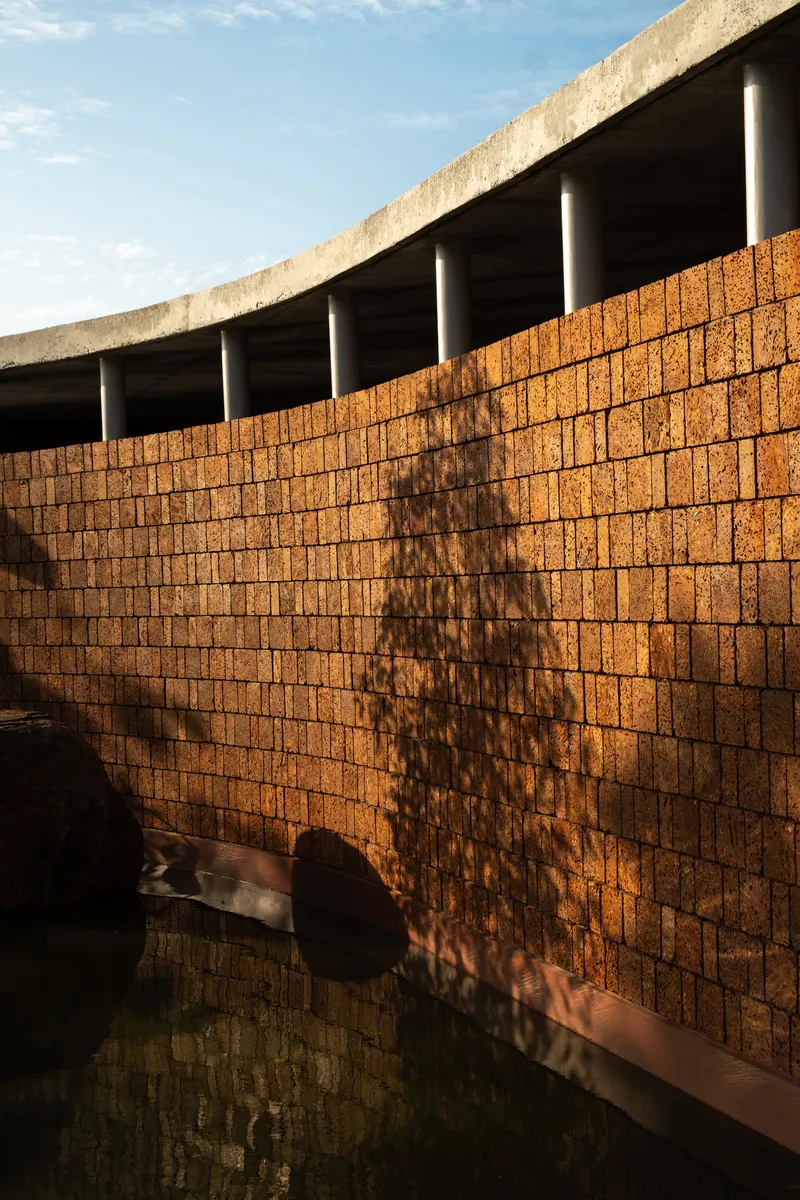 Curved laterite brick wall with tree shadow pattern beneath exposed concrete roof beam and columns