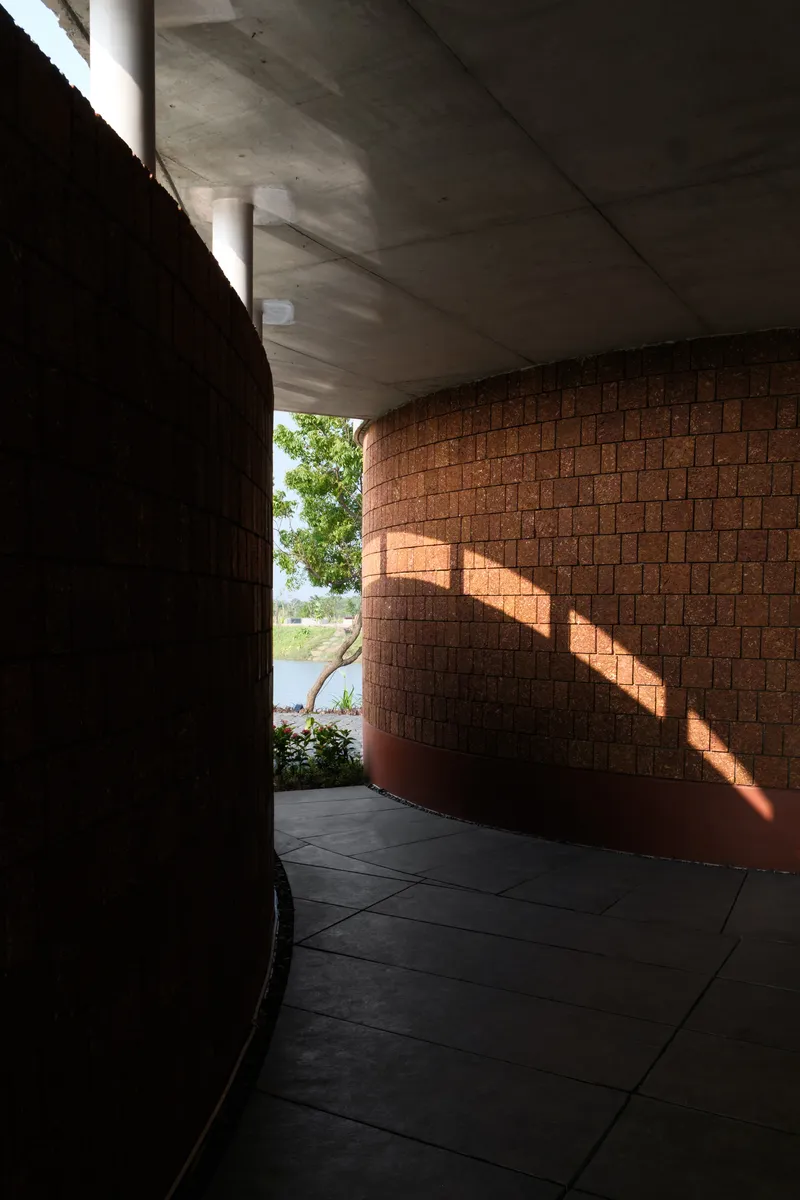 Curved interior corridor with laterite brick wall receiving striped sunlight through clerestory opening