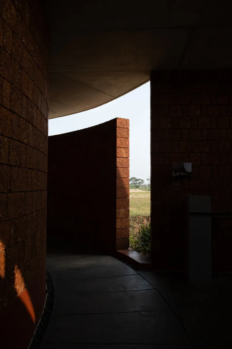 Interior corridor with curved concrete ceiling and compressed earth block walls framing a view to the landscape