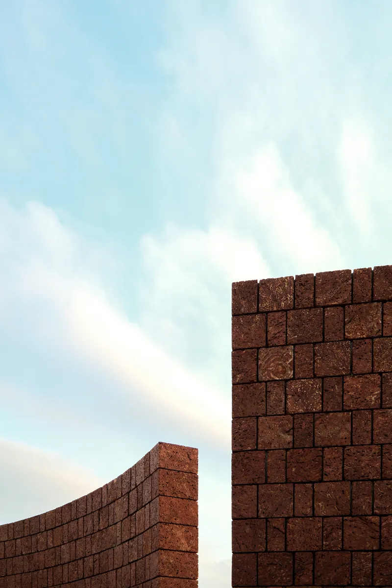Upward view of curved compressed earth block walls meeting against a pale sky