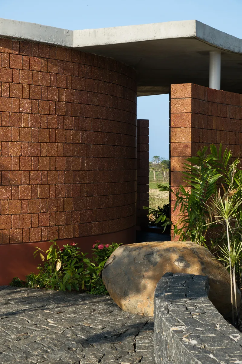 Courtyard framed by curved compressed earth block walls with a large boulder and plantings in afternoon light