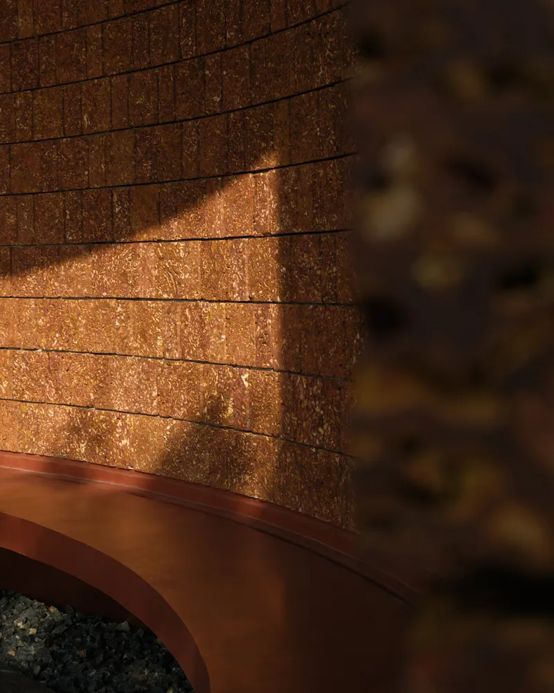 Detail of compressed earth block wall above a curved metal base in warm sunlight