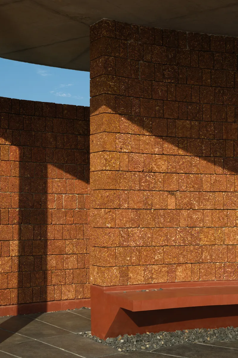 Textured rammed earth courtyard walls with geometric shadow patterns cast by the overhead canopy