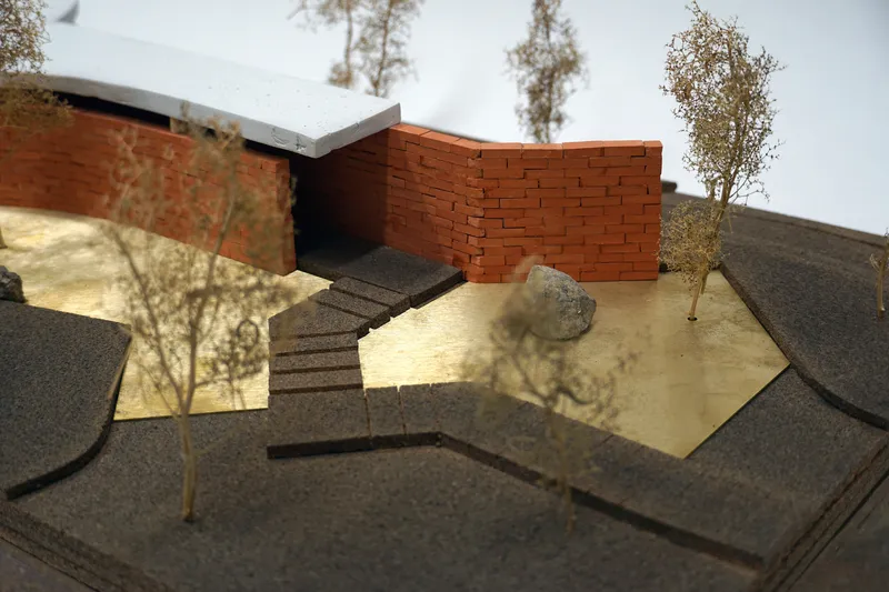 Physical model showing curved brick walls and angled staircase with miniature trees and rock